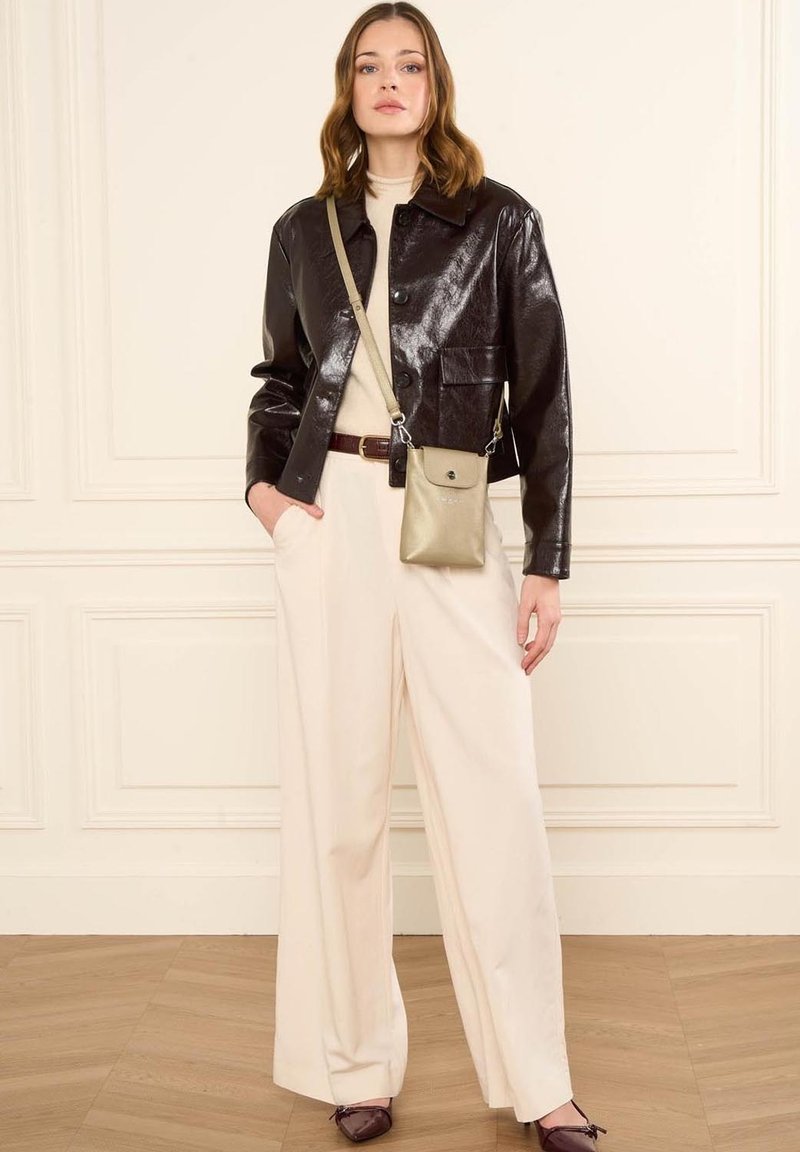 Femme portant une veste courte noire brillante, un col roulé beige, un pantalon large couleur crème, des chaussures bordeaux et un sac bandoulière beige.