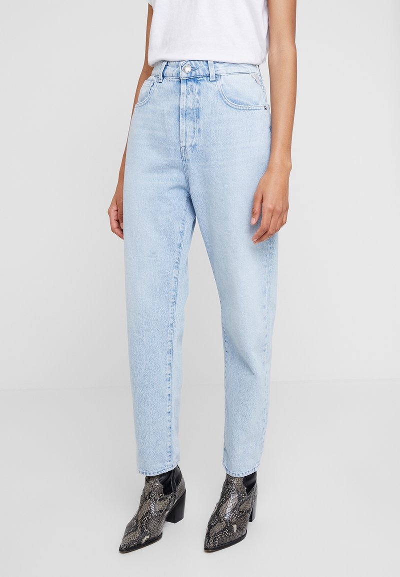 Jeans chiari a vita alta con gamba dritta, dotati di tasche frontali e chiusura con zip, abbinati a stivaletti neri texturizzati.