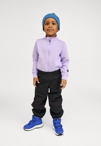 Lila zip-up jacka, svarta elastiska byxor med midja och blå sneakers med kardborreband. Outfiten har en mysig blå beanie.