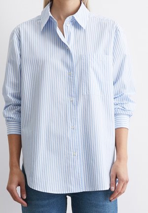 Person iført en løs, lyseblå og hvid vertikalt striped knap-up skjorte med lange ærmer og en brystlomme, kombineret med blå jeans.