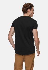 Zwarte t-shirt met korte mouwen en een ronde halslijn, met een gebogen onderkant, gedragen met lichtbruine broek, die een gladde stofstructuur laat zien.