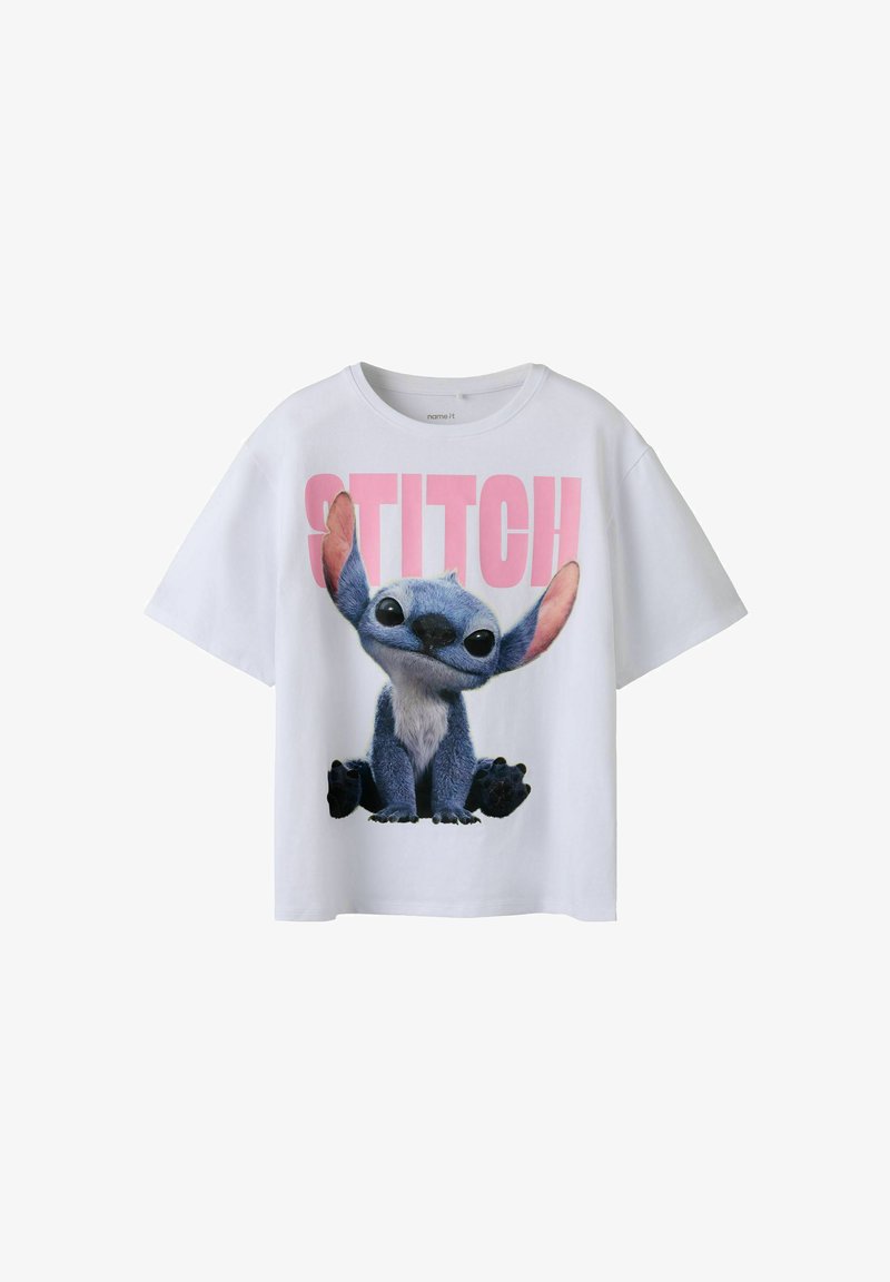 T-shirt en coton blanc arborant un personnage bleu aux grandes oreilles et aux yeux noirs, avec le texte imprimé "STITCH" en rose au-dessus. Manches courtes et coupe décontractée.