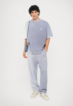 Lavender oversized T-shirt with white accents and logo, paired with matching tapered sweatpants. White sneakers complete the look.