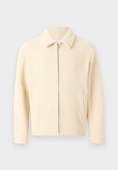 Ζακέτα με φερμουάρ σε εκχύμωχρο μπεζ χρώμα, πλεχτή με χοντρό πλέξιμο, με γιακά και μακριά μανίκια, εμφανιζόμενη πάνω σε λευκό φόντο.