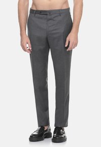 Pantaloni grigi su misura con taglio dritto, realizzati in un tessuto liscio, dotati di chiusura con bottone e tasche laterali. Indossati con scarpe nere.