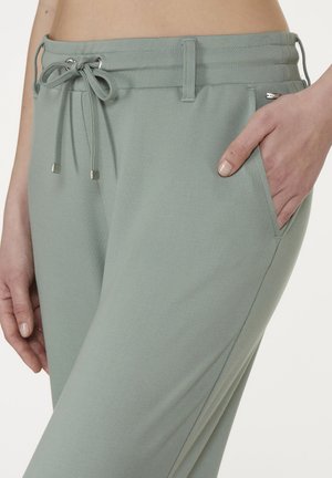 Light green jogger pants with drawstring waist, featuring a smooth texture and side pockets. Metallic accents on drawstring ends.