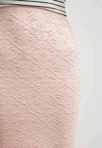 Svetle růžová sukně s texturou a vystouplým diamantovým vzorem, vyrobená z látky s měkkým pocitem, viditelná nad pruhovaným topem.
