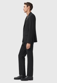 Completo nero composto da un blazer aderente e pantaloni a gamba dritta, caratterizzato da una texture liscia e un design semplice. Completato con scarpe nere.