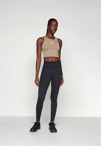 Αθλητικό τοπ σε μπεζ χρώμα και ψηλόμεσα μαύρα κολάν, και τα δύο από ελαστικό ύφασμα. Αθλητικά παπούτσια με υφή στην σόλα ολοκληρώνουν την εμφάνιση.