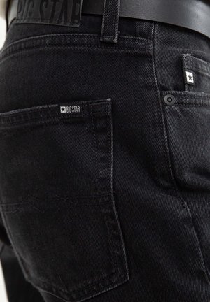 Juodi džinsai iš denim audinio su tekstūruotu pynimu, turintys Big Star etiketę ant galinio kišenės ir juodą odinį diržą su iškiltu ženklu.