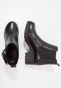 Botas negras de tobillo con cuero suave, paneles laterales elásticos, un tirador y un tacón de goma grueso con borde serrado.