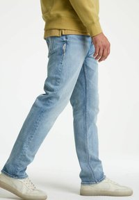 Hellblaue Jeans mit geradem Schnitt, die eine subtile Textur und Nähdetails aufweisen. Kombiniert mit cremefarbenen Sneakers.