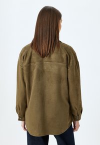 Camicia in suede verde oliva con maniche lunghe, vestibilità comoda, orlo arrotondato e dettagli con bottoni sui polsi. Texture liscia in tutto.