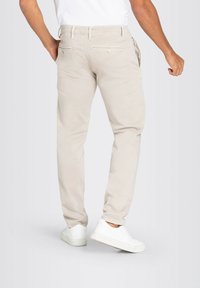 Beige tapered pants made of soft fabric, featuring a flat front, back pockets with button closure, and side pockets. White sneakers complement the look.