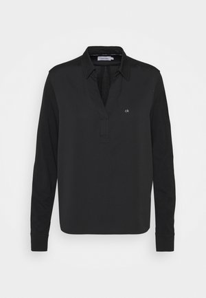 Schwarzes, langärmeliges Hemd mit Kragen, teilweiser Knopfleiste und kleinem weißen „ck“-Logo auf der linken Brust.