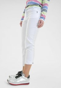 Witte cropped broek met een getailleerde pasvorm, voorzien van zijzakken en een opgerolde zoom. Gecombineerd met zilveren sneakers met zwarte veters en textuuraccenten.