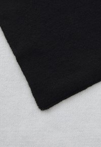 Sort stof med en blød tekstur overlapper et lysere, vævet strikmateriale, hvilket fremhæver kontrasterende farver og teksturer i et diagonalt layout.
