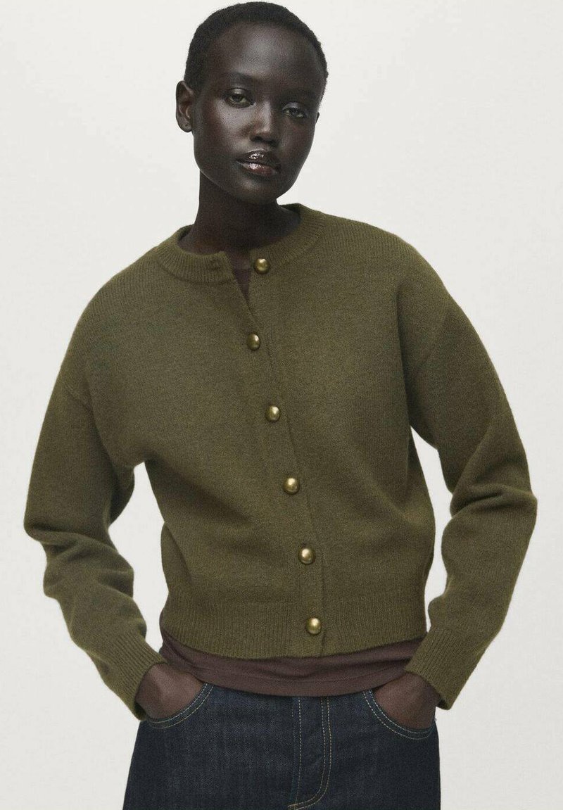 Cárdigan de punto verde oliva con escote redondo, que presenta botones dorados en el frente y puños acanalados, usado sobre una blusa marrón.