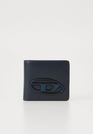 Portefeuille en cuir navy avec une texture lisse, présentant un accent logo ovale brillant bien en évidence en bleu foncé. Design plié à deux volets.