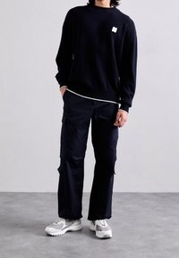 Marineblå striktrøje med ribbet hals og kant, kombineret med mørke cargobukser med sidelommer og atletiske sko med hvide detaljer.