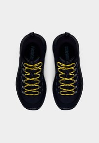 Mustad spordijalatsid, millel on tekstuurse pinnaga materjal, kollased paelad ja metallised detailid. Ümar ninaosa ja paks must välistald tagavad toe.