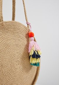 Sac rond en paille tressée avec des poignées tressées, décoré d'un pompon multicolore comprenant du rose, du jaune, du marine, du sarcelle et de l'orange.