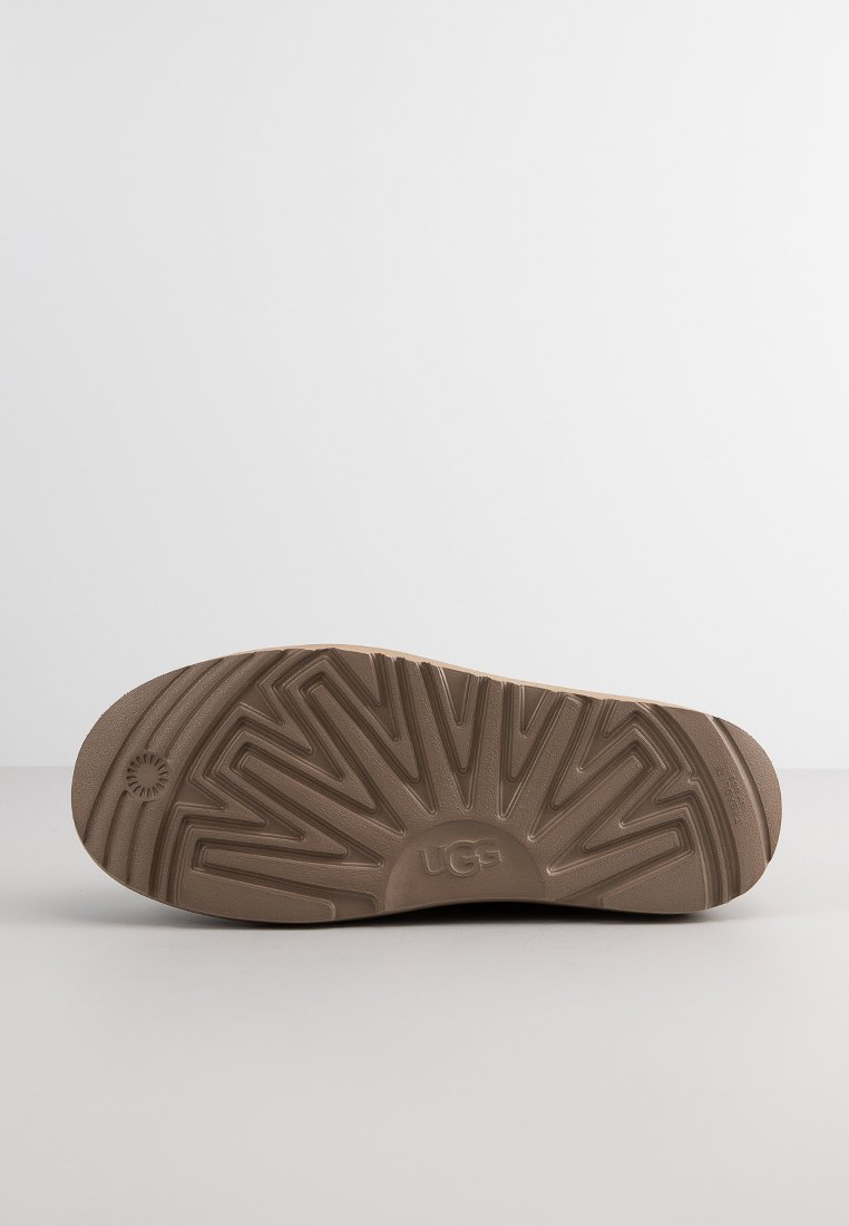 Brązowa gumowa podeszwa obuwia UGG z geometrycznym wzorem bieżnika i wytłoczonym logo na środku.