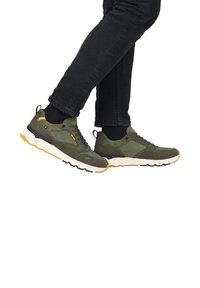 Sneaker verdi con un mix di materiali lisci e texture, caratterizzati da accenti gialli, suole nere e un design imbottito per il comfort.
