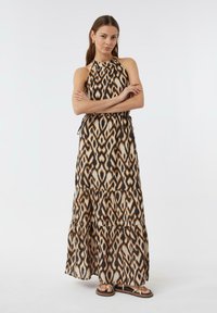 Maxi sukienka w tribalowy wzór w brązowych, beżowych i czarnych kolorach. Posiada halter neck, warstwowy krój oraz podkreśloną talię. Noszona z płaskimi sandałami.
