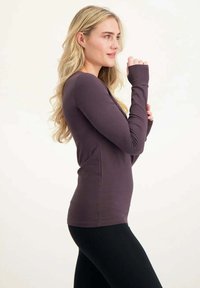 Langärmliges, eng anliegendes Oberteil aus dunkelviolettem Stoff mit glatter Textur und Daumenlöchern an den Bündchen, kombiniert mit schwarzen Leggings.