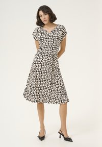 Robe à motifs noir et crème avec des manches courtes, décolleté en V et taille cintrée, dotée d'une jupe fluide et d'une texture de tissu lisse.