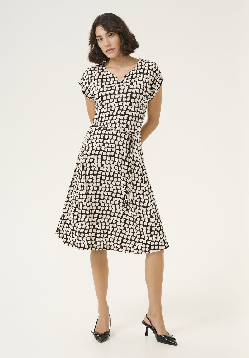 Robe à motifs noir et crème avec des manches courtes, décolleté en V et taille cintrée, dotée d'une jupe fluide et d'une texture de tissu lisse.