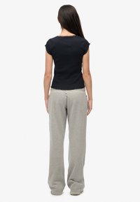 Czarny top z krótkim rękawem o fakturowanym splocie i falowanym brzegu, zestawiony z luźnymi szarymi spodniami dresowymi z kieszeniami i swobodnym krojem.