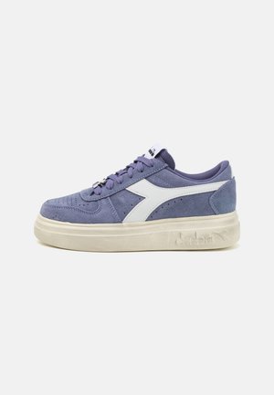Sneaker in suede viola con dettagli in pelle bianca, punta rotonda, lacci piatti e suola in gomma chunky color crema. Logo del marchio sul lato.