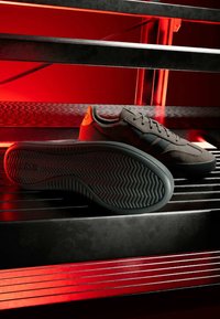 Černé tenisky s texturovaným svrškem, zdobené kontrastními tmavými pruhy, gumovou podrážkou a vzorem rybí kosti na spodní straně.