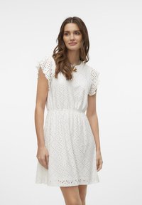 Vestito bianco in cotone con maniche corte a rouches, disegni in pizzo tagliato al laser e vita elastica, che si apre a campana dalla vita.