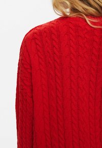 Maglione rosso lavorato a maglia con un motivo a cable testurizzato. Presenta un colletto rotondo e una vestibilità rilassata, che mette in mostra un colore vivido e un materiale morbido.