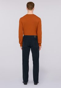 Camisa de manga larga color naranja quemado, ajustada, combinada con pantalones de un azul marino oscuro. Los pantalones tienen dos bolsillos traseros y una cinturilla negra texturizada.