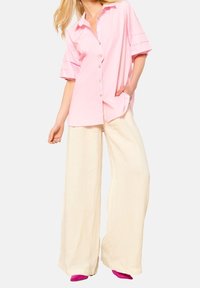 Light pink short-sleeve button-up shirt with a pocket and layered sleeves, paired with cream wide-leg pants and pink footwear.