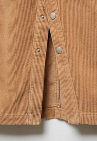 Tessuto in velluto a coste marrone con righe verticali, dotato di chiusura laterale con bottone. Texture liscia con cuciture visibili e bottoni a pressione in metallo.