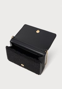Borsa nera con un frontale in tessuto nero con effetto peloso, retro in pelle liscia, accessori dorati e tracolla a catena. Apertura con chiusura a scatto.
