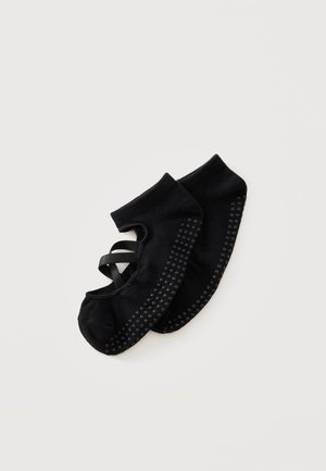 Calcetines de ballet negros con agarres antideslizantes en las suelas y tiras elásticas cruzadas para un ajuste seguro, colocados planos sobre un fondo blanco.