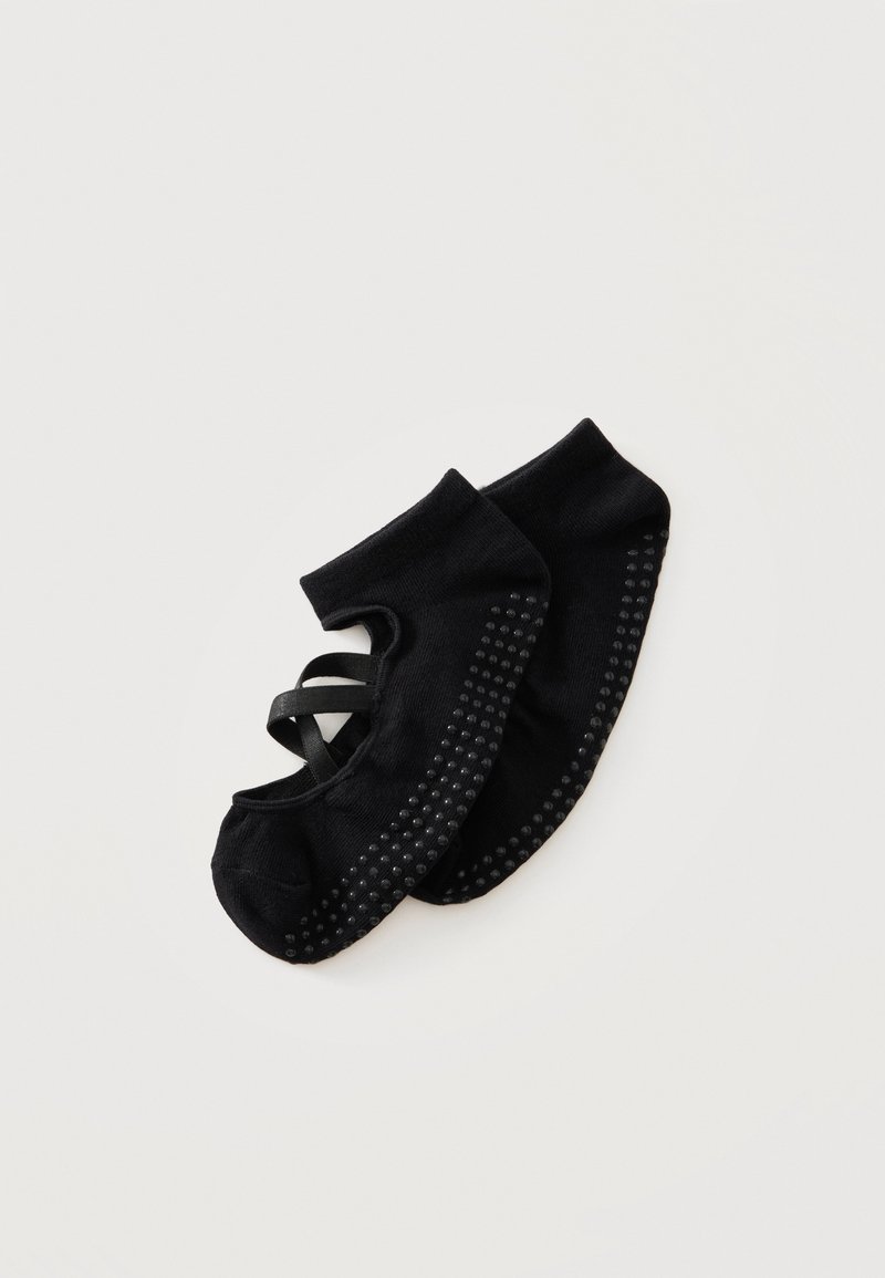 Chaussettes de ballet noires avec des grips antidérapants sous les semelles et des sangles croisées élastiques pour un bon maintien, posées à plat sur un fond blanc.