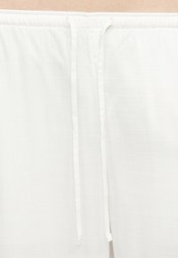 Κοντινό πλάνο στη μέση λευκού ενδύματος με δύο λεπτά, χαλαρά κορδόνια που κρέμονται στο κέντρο.