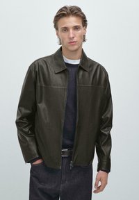 Mörkgrön läderjacka, dragkedja fram, spridd krage, långa ärmar, slät textur, kombinerad med en marinblå tröja och denimjeans.