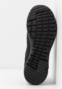 Sole di scarpa sportiva nera con un modello di trazione multidirezionale, superficie testurizzata e marchio Skechers su un lato liscio.