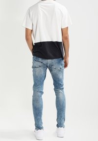 Short-sleeve, color-block t-shirt in white and navy, paired with light-wash denim jeans with a slim fit and distressed details. White sneakers.