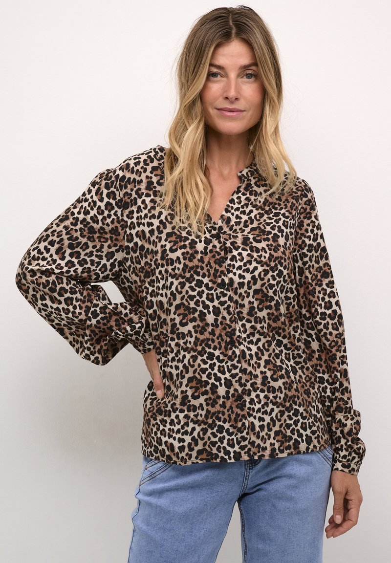 Leopardmönstrad skjorta i beige, brunt och svart; långa ärmar; knappstängning framtill; mjukt material; avslappnad passform; matchad med blå denimjeans.