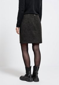 Tummanharmaa hame, joka on valmistettu teksturoidusta kankaasta, takana on vetoketju. Yhdistetty mustiin nilkkasaappaisiin ja mustiin sukkahousuihin. Yksinkertainen muotoilu.