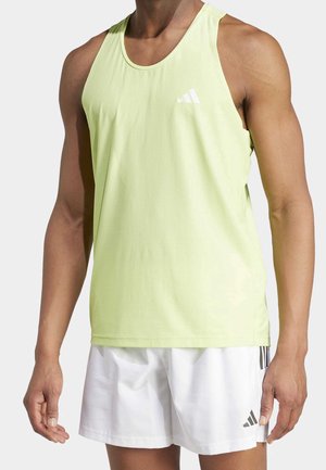 Homme athlétique portant un débardeur Adidas vert clair sans manches et un short blanc Adidas, debout devant un fond uni.